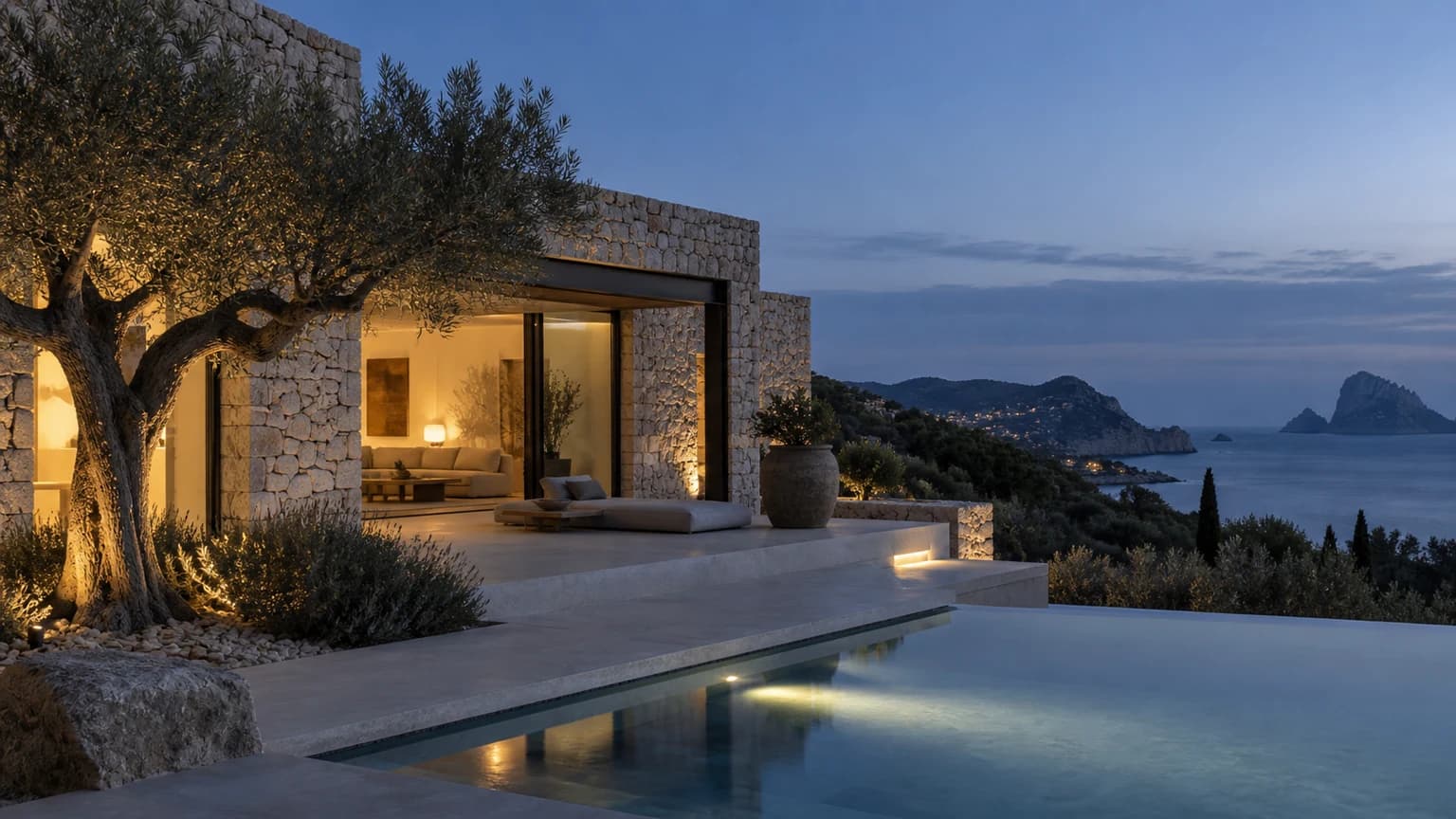 Mediterrane Villa bei blauer Stunde mit warm beleuchteten Innenräumen, Olivenbaum und Meerblick