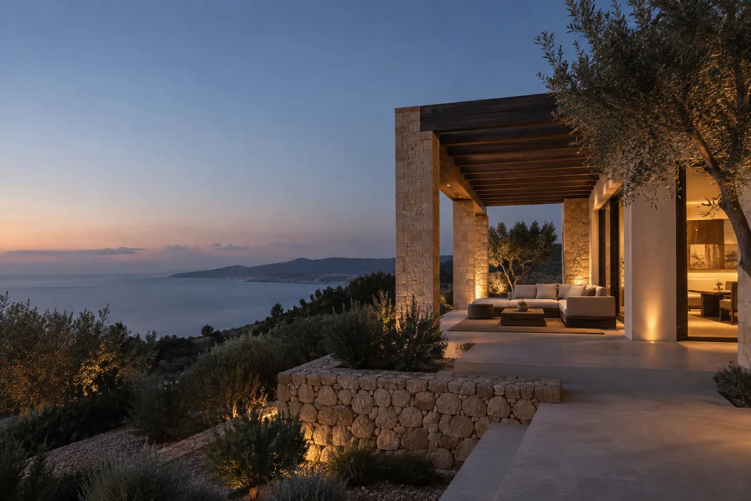 Mediterrane Natursteinvilla mit warmer Beleuchtung und Blick auf die Küste bei blauer Stunde